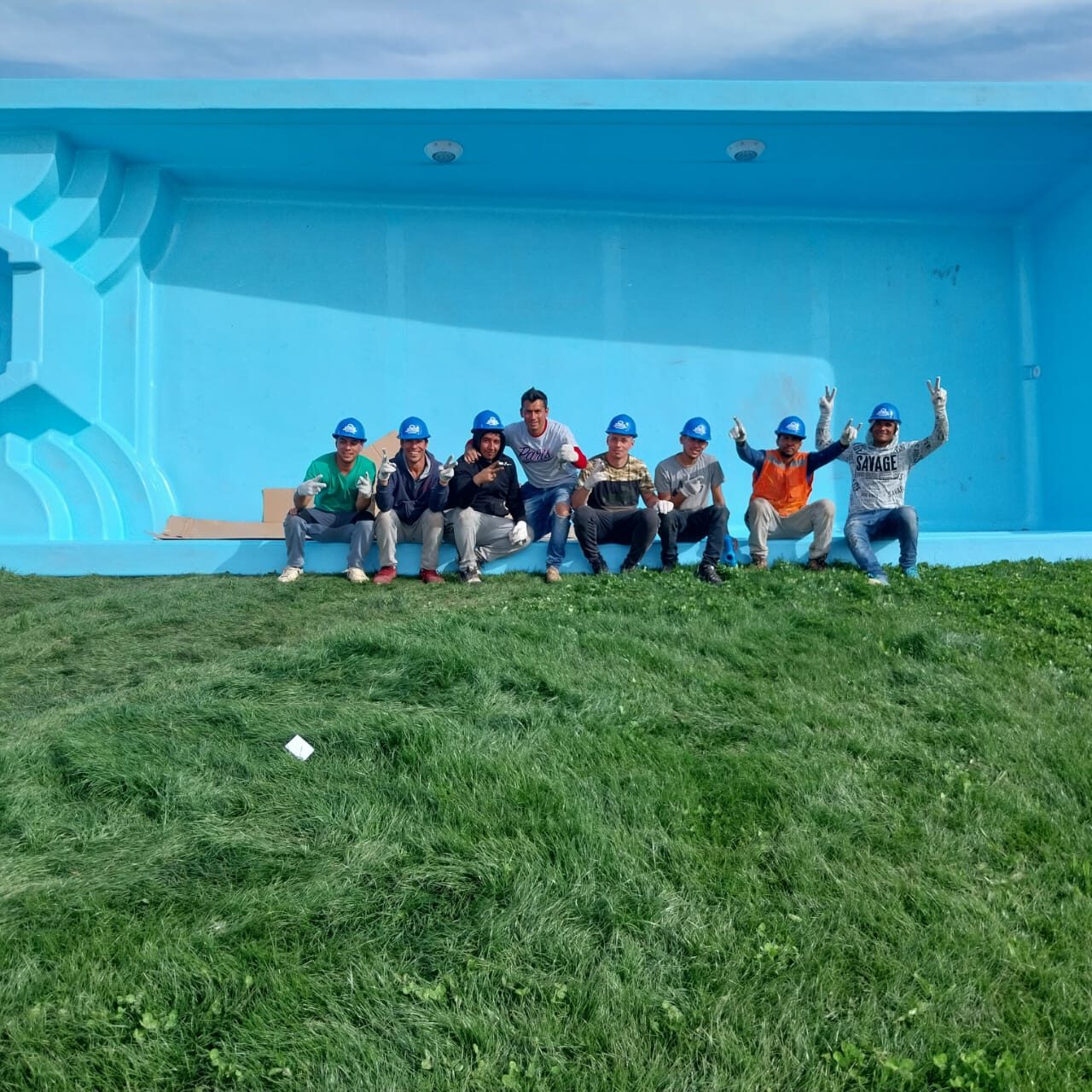 Equipo completo de instaladores ALB-KEV dentro del casco de una piscina de fibra de vidrio, con cascos de seguridad