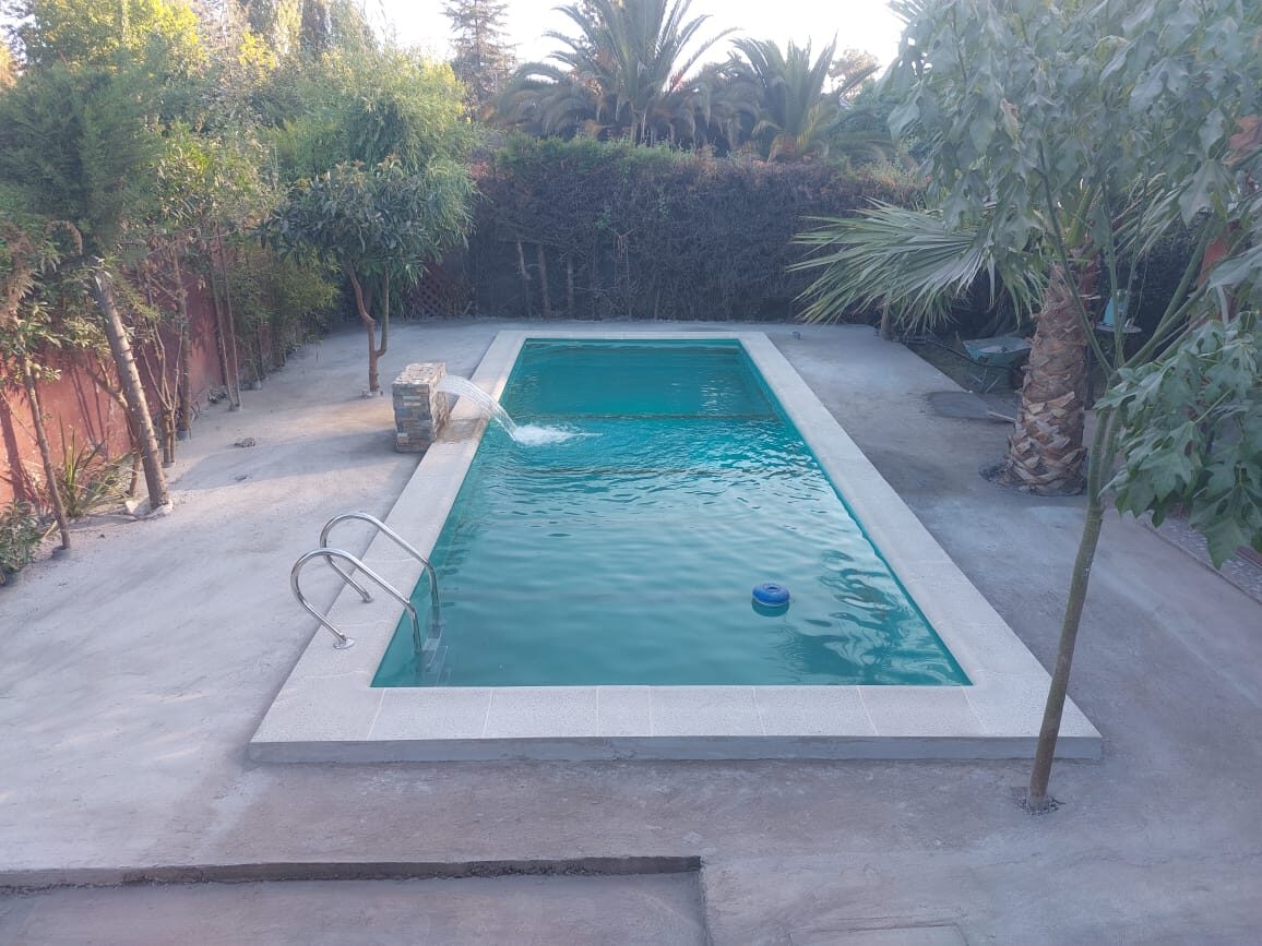 Piscina mediana ALB-KEV con cascada decorativa rodeada de palmeras, ideal para uso familiar
